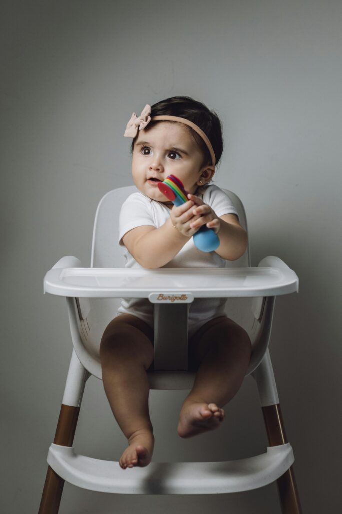 Charming portrait of a baby girl in a high chair holding a colorful toy indoors.